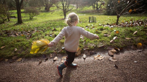 Girl running in the garden with a large autumnal leaf at Killerton
